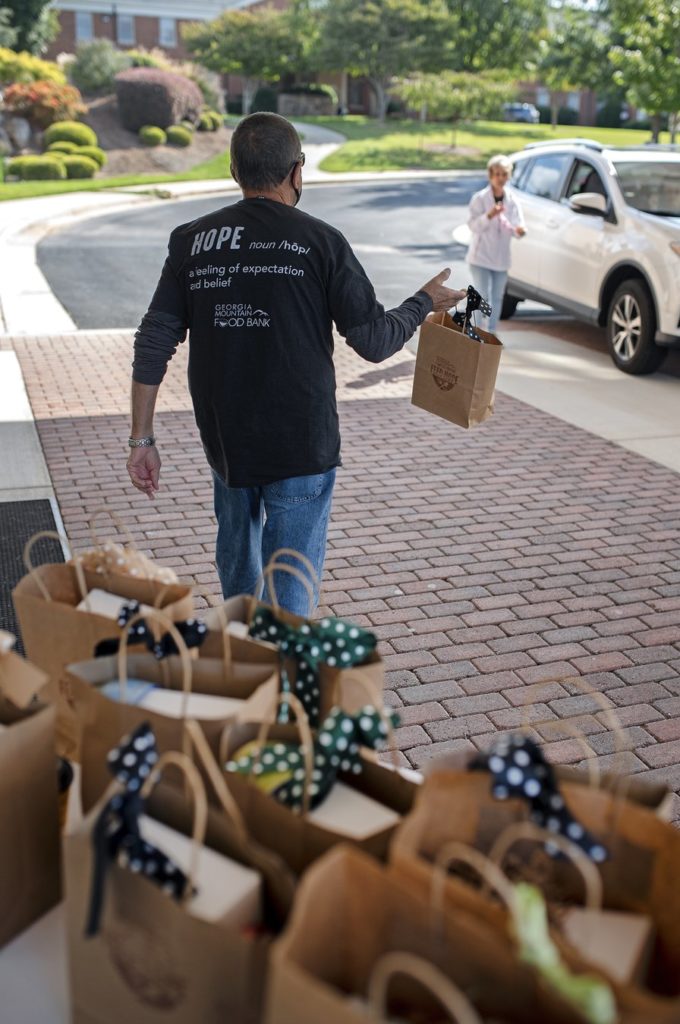 Man passing out a brown paper bag to a parked car